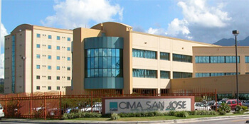 Picture of CIMA Hospital – San José, Costa Rica, a tall, large 3-story building, tan in color, with a large entrance sign saying CIMA - San José.